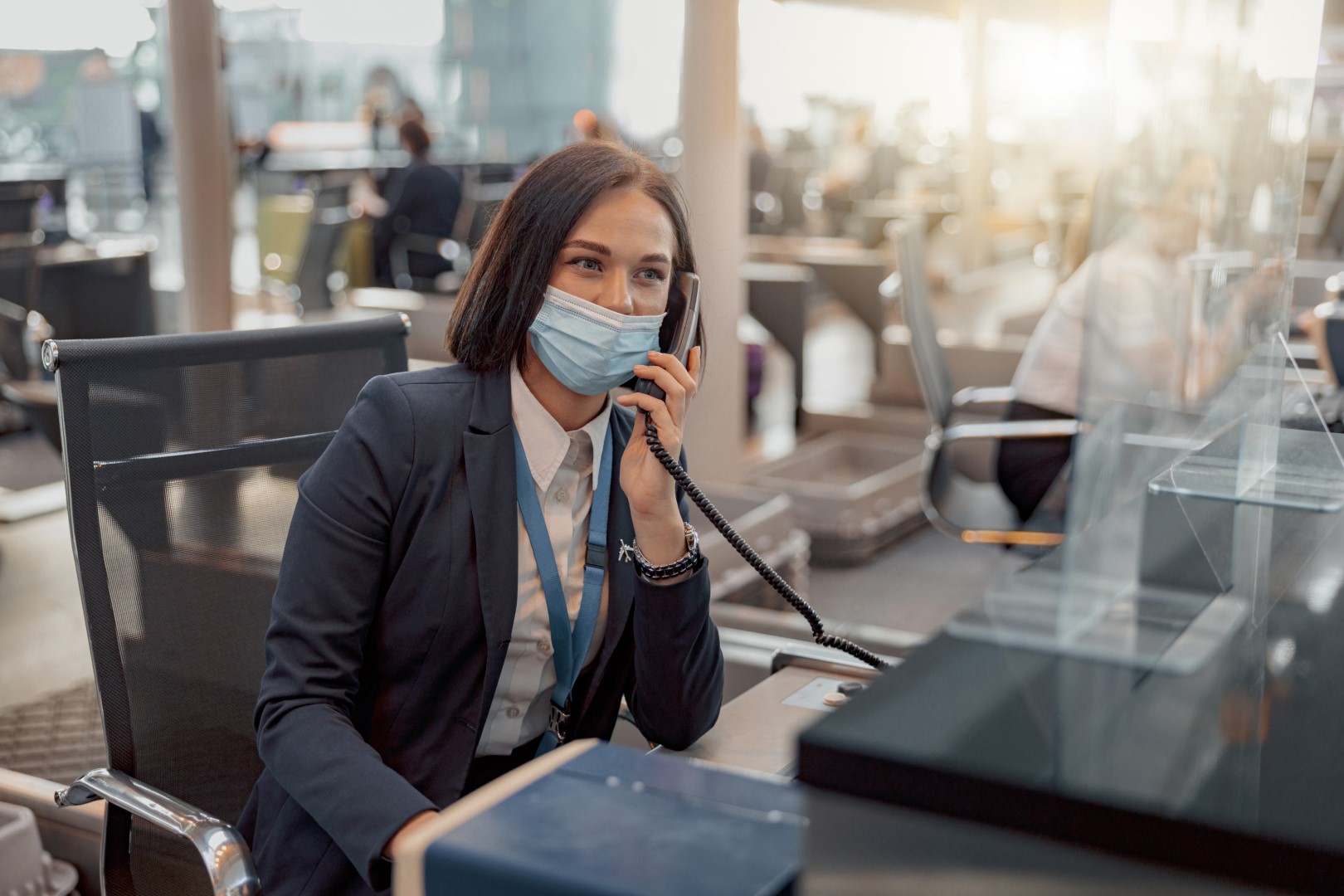 Woman in protective mask working in the control service and talking on the phone in airport terminal